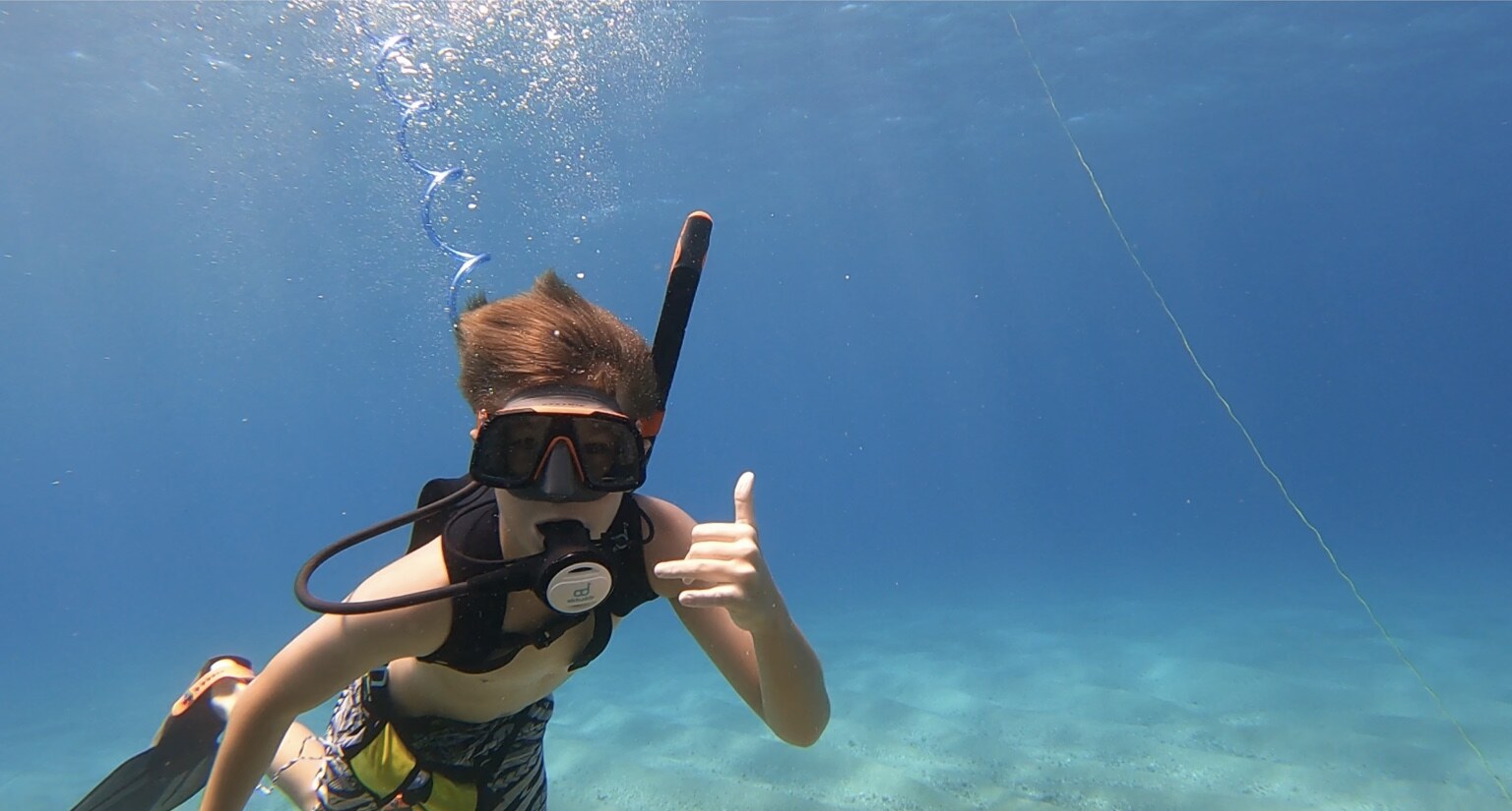 A young tankless diver giving a shaka during a guided underwater adventure in clear Maui water